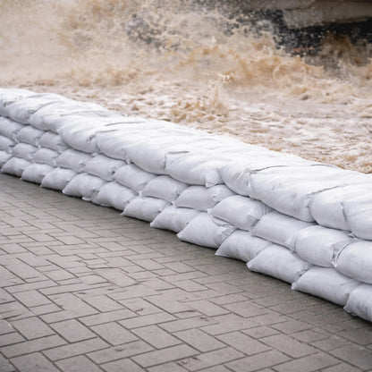 Stack of white sandbags on a stone pavement with water flowing in the background