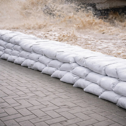 Stack of white sandbags on a stone pavement with water flowing in the background